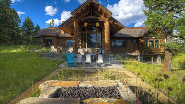 A log cabin with a stone foundation, wooden exterior, and a covered patio with outdoor seating. - Spanish Peaks Mountain Home - Big sky (Big Sky)