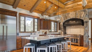 A modern kitchen with a large island, wooden cabinets, and a stone fireplace. - Spanish Peaks Mountain Home - Big sky (Big Sky)