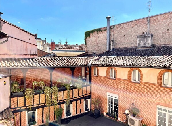 A courtyard with a brick building, tiled roof, and potted plants. - Le Virtuose - Dans l'hypercentre de Toulouse (Toulouse)
