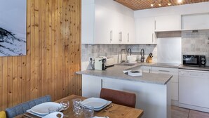 A modern kitchen with wooden paneling, white cabinets, and a dining area with a wooden table and chairs. - Spacious duplex for 9, central Val Thorens (Val Thorens)