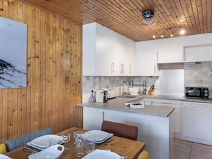 A modern kitchen with wooden paneling, white cabinets, and a dining area with a wooden table and chairs.
