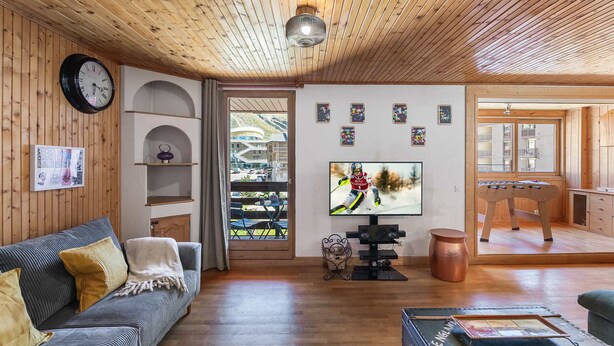 A cozy living room with a wooden ceiling, a sofa, a television, and a foosball table. - Spacious duplex for 9, central Val Thorens (Val Thorens)