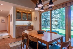 A modern kitchen with wooden cabinets, a dining table with chairs, and a large window offering a view of the outdoors.