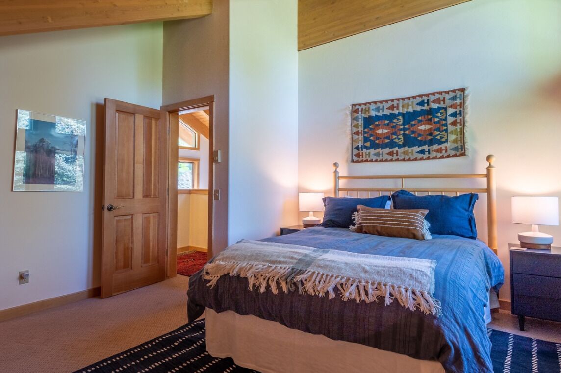Une chambre à coucher comprenant un lit, des tables de chevet, une porte, une courtepointe accrochée au mur et un tapis.