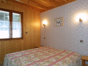 Una camera da letto con pareti in legno, una coperta con motivo floreale e due luci fissate al muro.