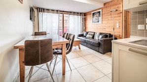 Une cuisine moderne avec un mur recouvert de carreaux, un coin repas en bois avec une table et des chaises, et un salon avec un canapé et des coussins.
