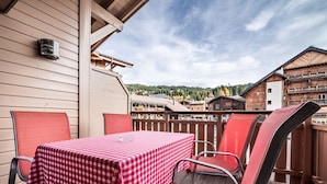 Une terrasse avec une table à carreaux et des chaises rouges, donnant sur un village niché dans les montagnes.