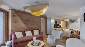 Ein modernes Wohnzimmer mit einer Wand in Holzoptik, einer Couch mit Kissen, einem runden Couchtisch mit Gläsern und einem Essbereich im Hintergrund.