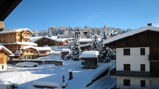 A snow-covered village with wooden buildings, a ski lift, and a clear blue sky.