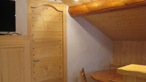 A wooden interior with a dining table and chairs, a wooden cabinet, and a television on a stand.