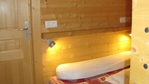 A wooden cabin room with a bed, a door, and a light fixture.