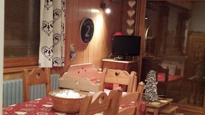 A cozy dining area with a table set for four, wooden chairs, a television on a stand, and a small Christmas tree. - Cozy family apartment in Les Gets with Wi-Fi, garage, 2 bedrooms (Les Gets)