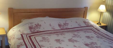 A bed with a wooden headboard, a white and red patterned bedspread, and a bedside lamp on a wooden nightstand.
