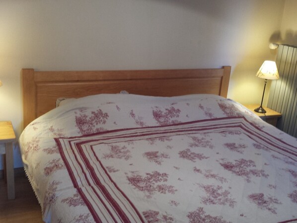 A bed with a wooden headboard, a white and red patterned bedspread, and a bedside lamp on a wooden nightstand.