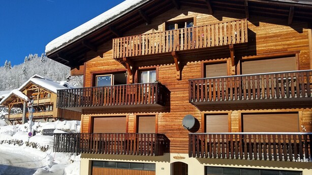 A wooden chalet with balconies, a garage, and a snow-covered roof. - Cozy family apartment in Les Gets with Wi-Fi, garage, 2 bedrooms (Les Gets)