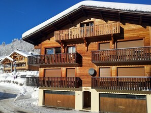 A wooden chalet with balconies, a garage, and a snow-covered roof.