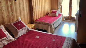 Habitación de cabaña de madera con dos camas, cada una con colcha roja y almohadones decorativos.
