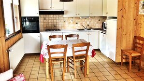 Una cocina compacta con gabinetes blancos, salpicadero de azulejos, una mesa de comedor con sillas y una lámpara colgante.