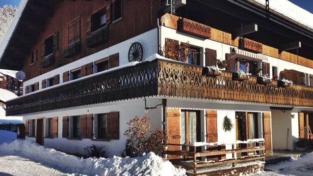 Un edificio de dos pisos con balcones de madera y el suelo cubierto de nieve.
