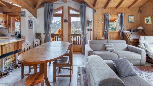 A wooden cabin interior with a dining table, chairs, a sofa, and a window overlooking a snowy landscape. - Family Chalet for 8 in Courchevel Le Praz with Wifi (Courchevel)