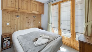 A bedroom with a large bed, wooden wardrobe, and a window with curtains. - Family Chalet for 8 in Courchevel Le Praz with Wifi (Courchevel)