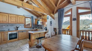 A wooden interior with a kitchen, dining area, and a view of mountains. - Family Chalet for 8 in Courchevel Le Praz with Wifi (Courchevel)