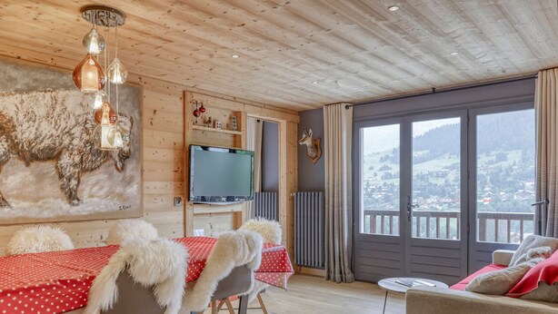 A cozy cabin interior with a dining table, chairs, a sofa, and a TV.