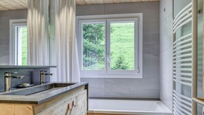 A modern kitchen with a wooden countertop, two sinks, and a window overlooking a green landscape.