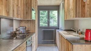 A modern kitchen with wooden cabinets, a built-in oven, and a window with a view of trees.