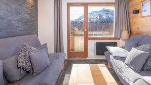 A modern living room with two grey sofas, a wooden accent wall, a large window with a mountain view, and a fireplace. - Charming renovated 2-room cabin for 6 with balcony in Avoriaz (Avoriaz)