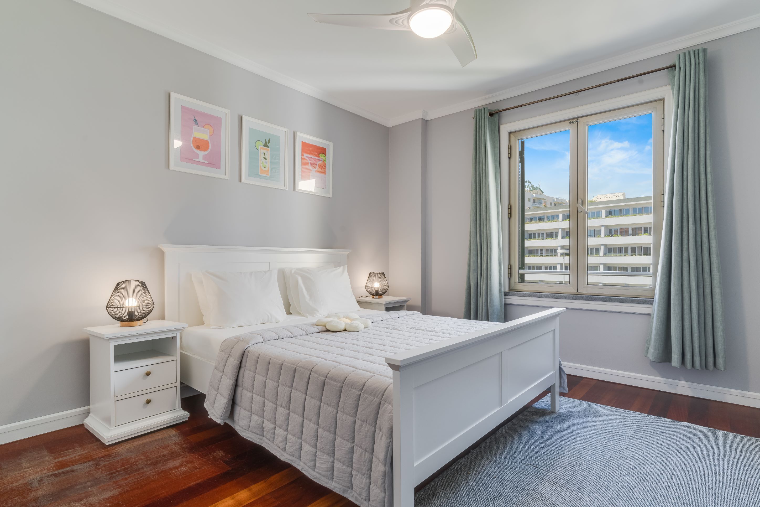 A bedroom with a bed, nightstands, a window with curtains, and wall art.