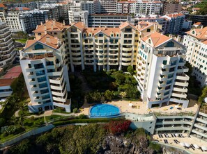 A high-rise residential building with multiple balconies, a swimming pool, and surrounding greenery. - Apartment Falesia Paradise (Funchal)