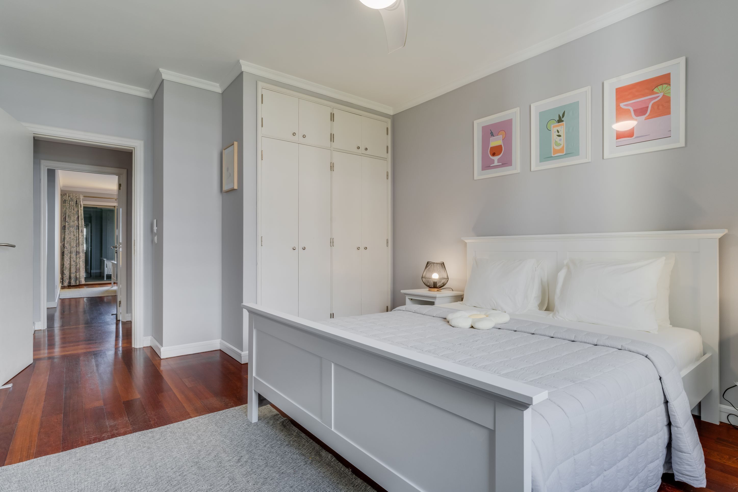 A bedroom with a large bed, a wardrobe, a nightstand with a lamp, and three framed pictures on the wall.