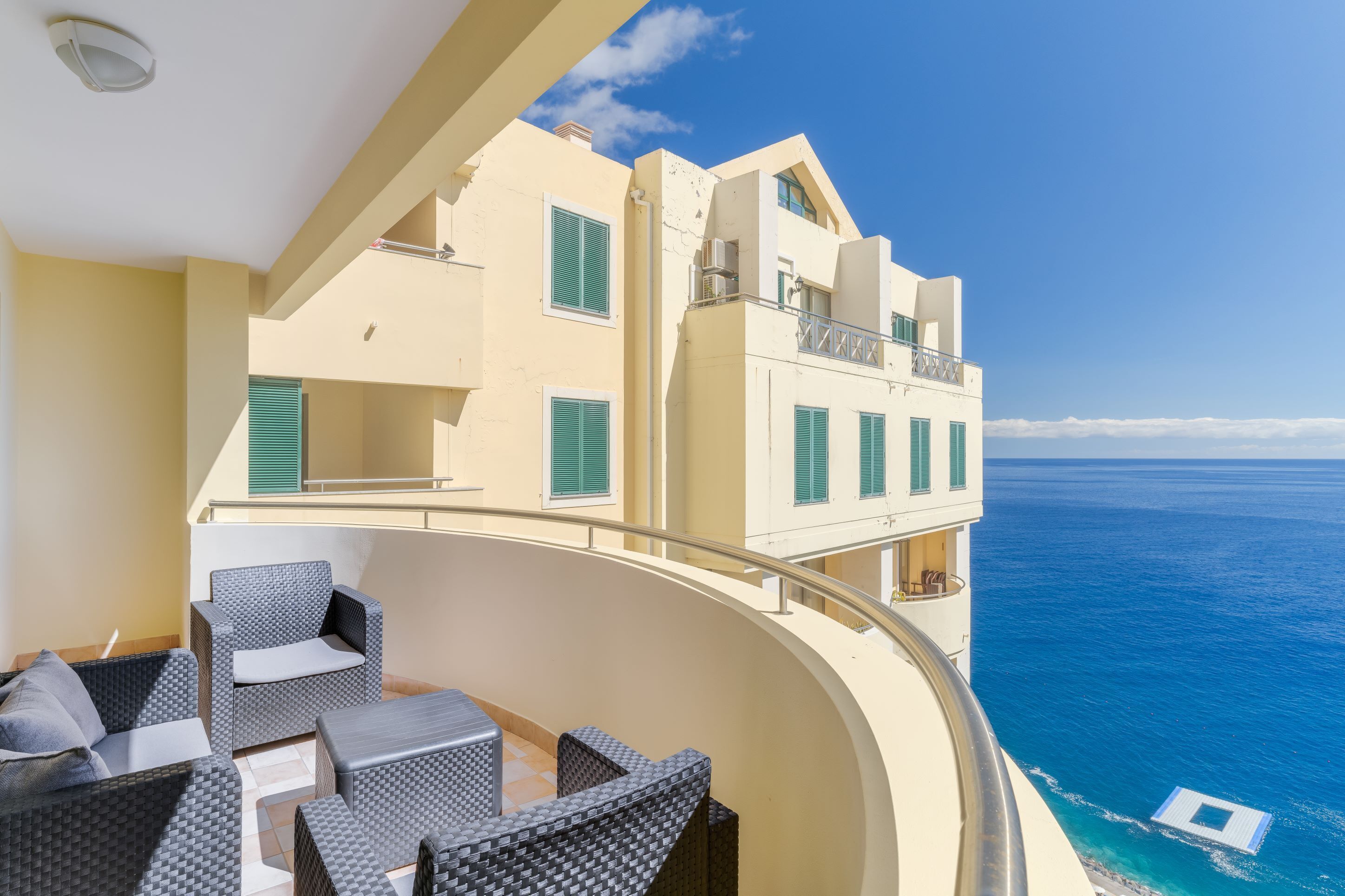 A balcony with wicker furniture overlooking a clear blue sea.