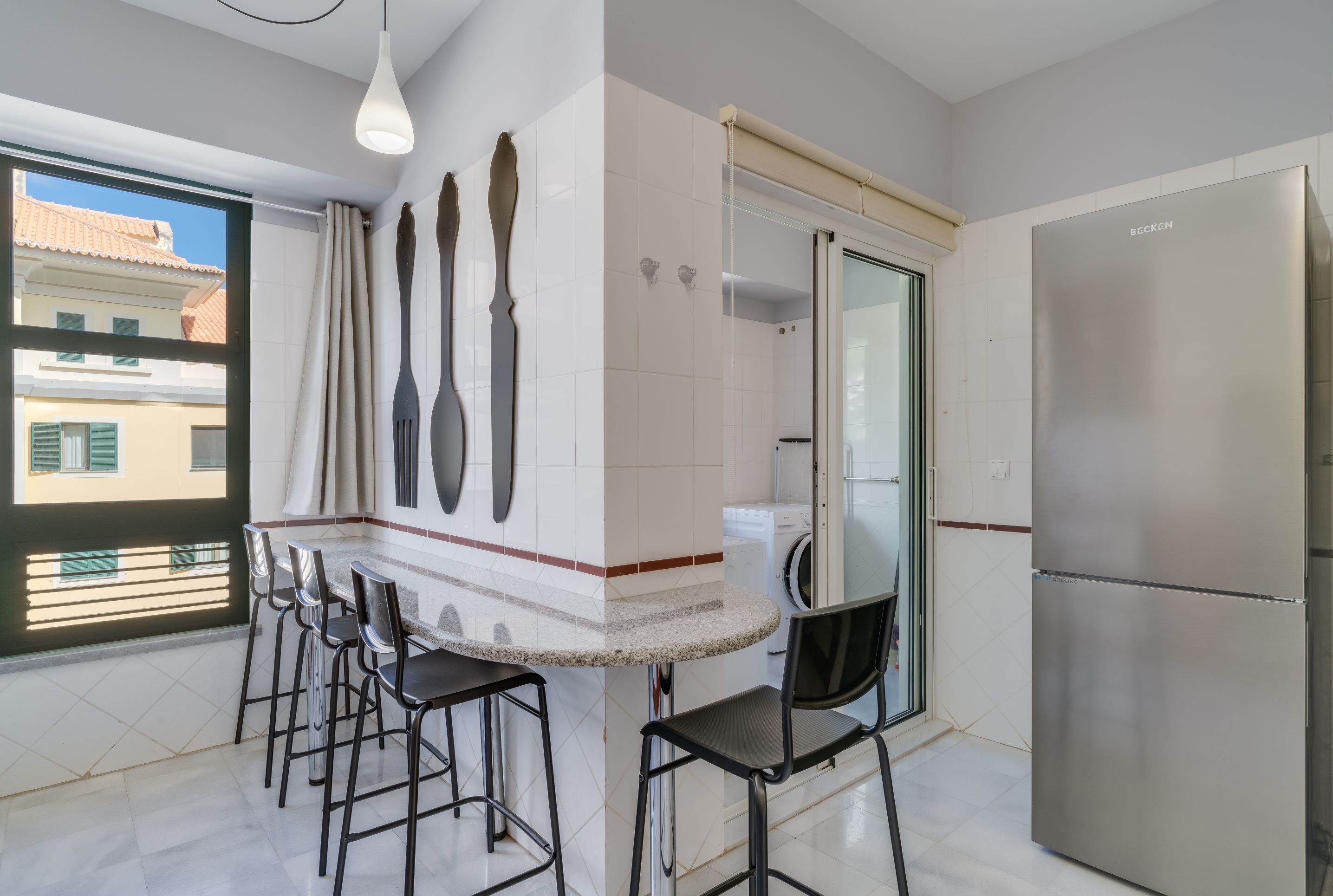 Una cucina moderna con frigorifero in acciaio inossidabile, forno integrato e zona pranzo con sgabelli da bar.