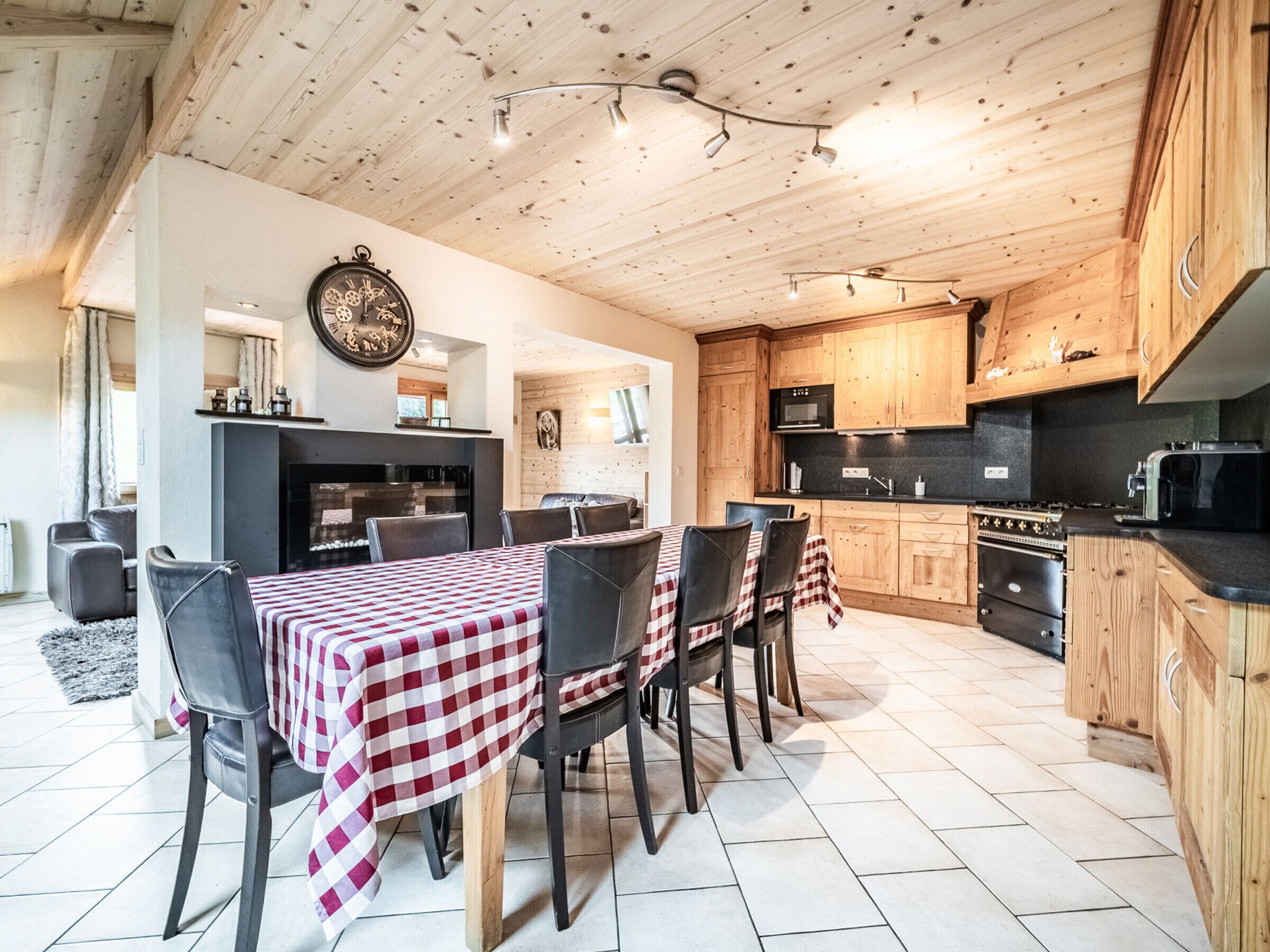 A spacious kitchen with wooden cabinets, a dining area with a checkered tablecloth, and a large wall clock.