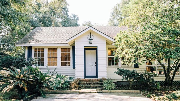 A single-story house with a white exterior, a black front door, and a small porch with a lantern.