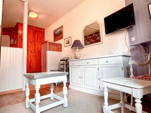 A room with a white table, a white cabinet, a television mounted on the wall, and a red curtain.