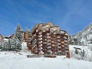 A multi-story hotel with balconies, surrounded by snow-covered trees and a clear blue sky.