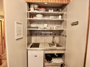 A compact kitchenette with a built-in stove, sink, and storage shelves.