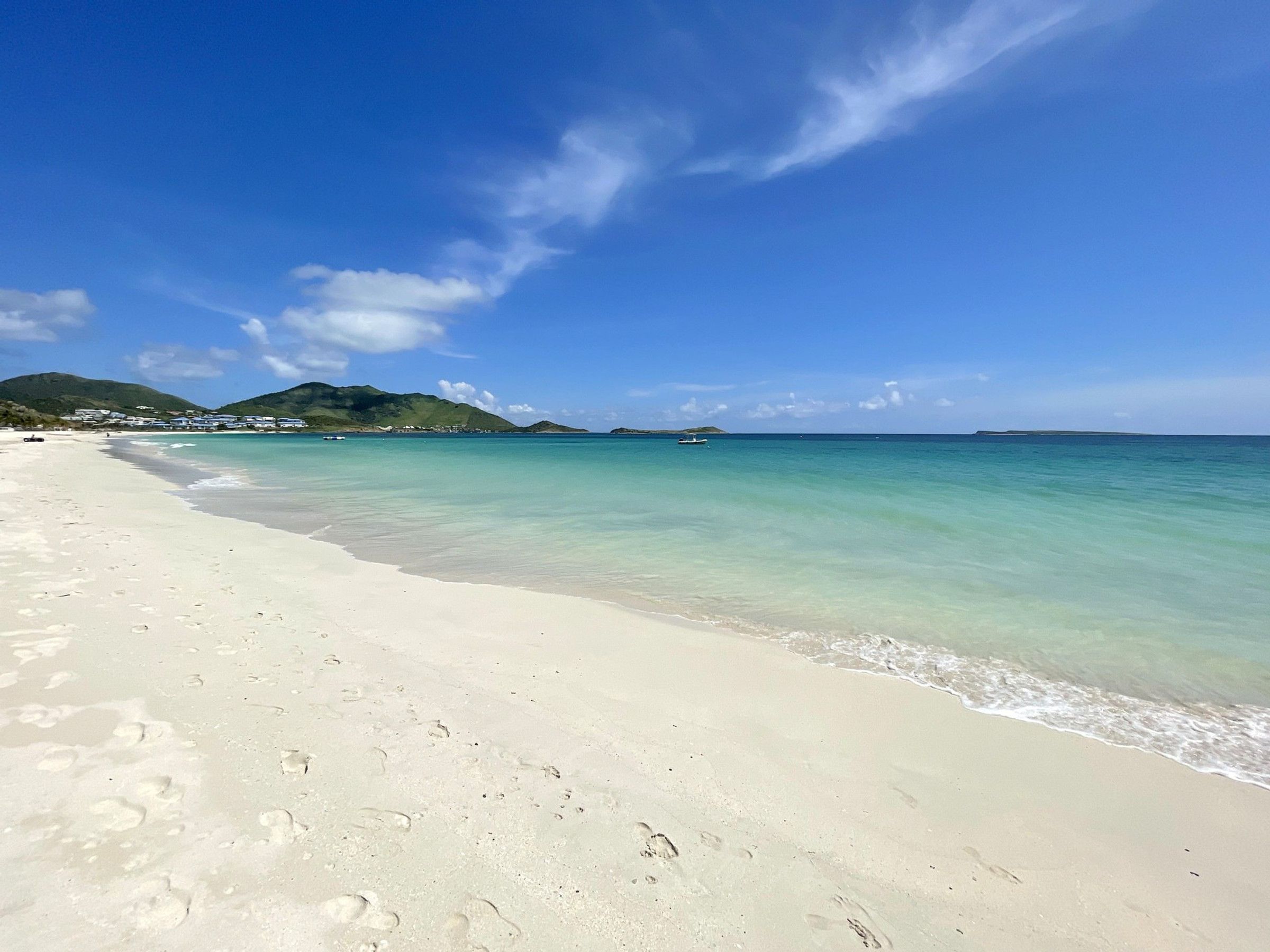 A beach with clear turquoise water, white sand, and a mountain in the background.