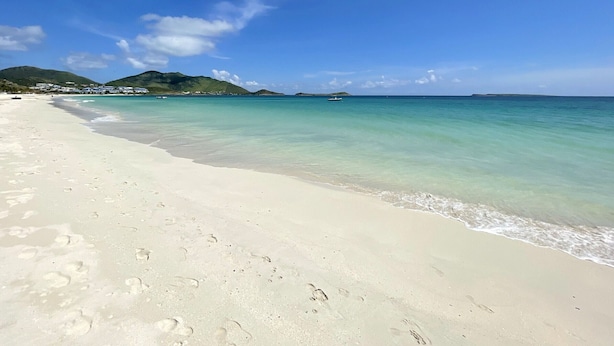 A beach with clear turquoise water, white sand, and a few footprints.
