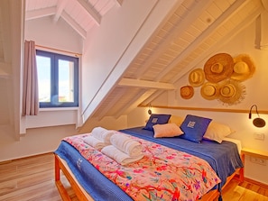 A bedroom with a sloped ceiling, a bed with a floral bedspread, and a window with curtains.