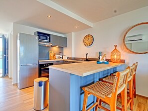 A modern kitchen with a central island, stainless steel appliances, and a large wall clock.