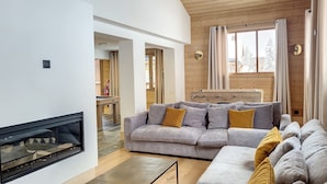 Ein modernes Wohnzimmer mit Kamin, grauen Sofas mit gelben Kissen, Holzwänden und einem großen Fenster mit Vorhängen.