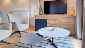 Ein modernes Wohnzimmer mit einem Flachbildfernseher, zwei Sesseln, einem Couchtisch und einer dekorativen Vase.