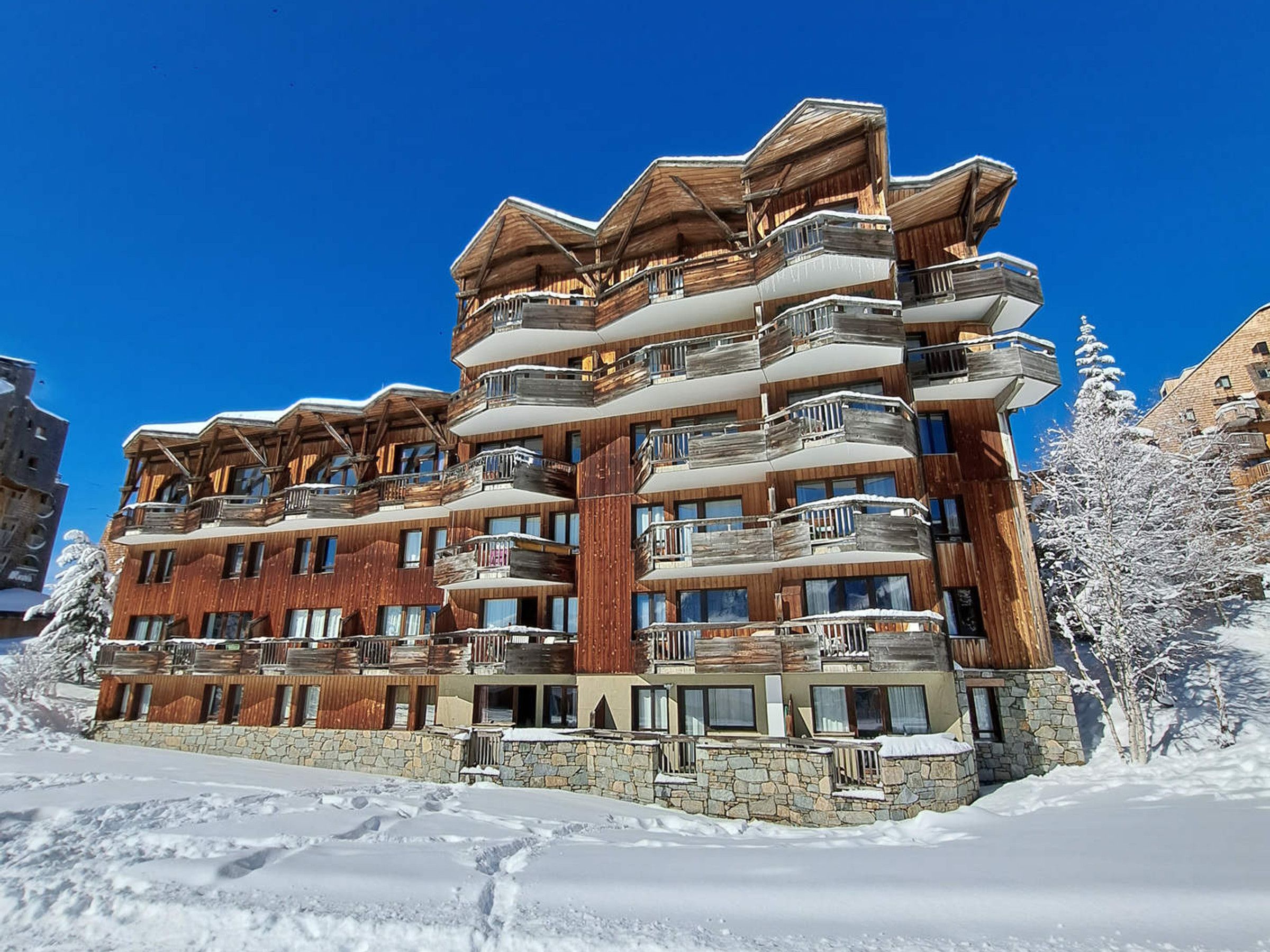 Un hotel a più piani con balconi in legno e facciata in pietra, immerso nella neve.