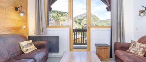 A cozy room with two leather sofas, a wooden table, and a large window with a view of a mountainous landscape.