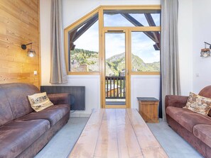A cozy room with two leather sofas, a wooden table, and a large window with a view of a mountainous landscape.