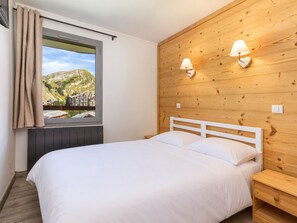 A bedroom with a bed, a window with curtains, a wooden wall, and two wall-mounted lamps.